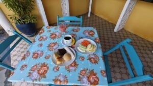 Mesa farta de café da manhã com tapioca, bolos regionais, frutas tropicais e café servido em mesa com toalha florida.