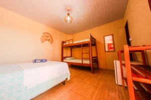 Suíte Familiar Conforto - Acomodações Suíte familiar na Pousada Costa do Mar com cama de casal, beliche de madeira, frigobar e banheiro com água quente em Luís Correia, PI.