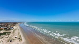 Foto aérea panorâmica mostrando a ampla faixa de areia da Praia de Peito de Moça em Luís Correia, ideal para caminhadas relaxantes.